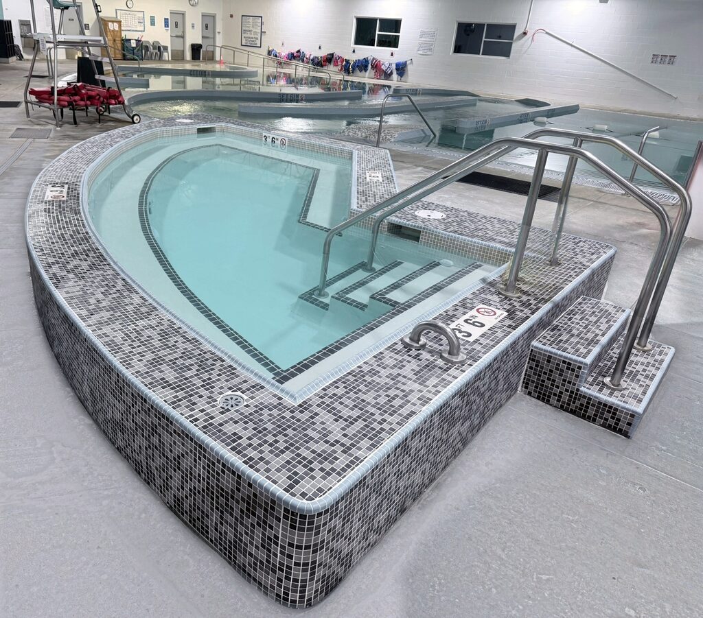 Indoor mosaic-tiled therapy pool with stainless steel handrails and entry steps